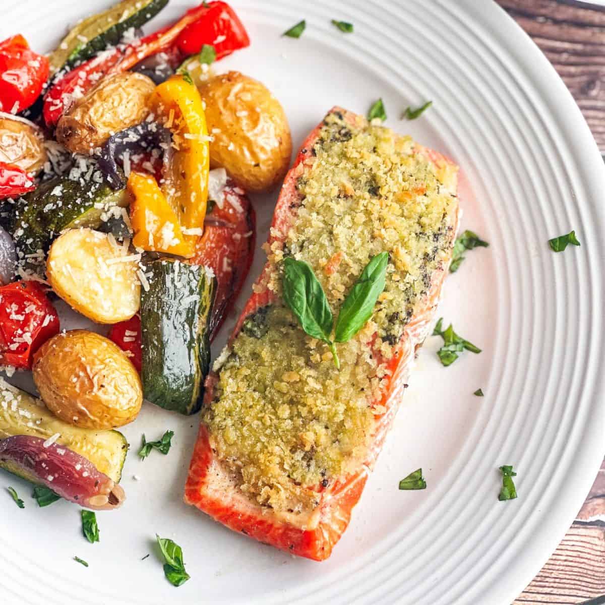 Pesto crusted salmon with roasted vegetables on a white plate.