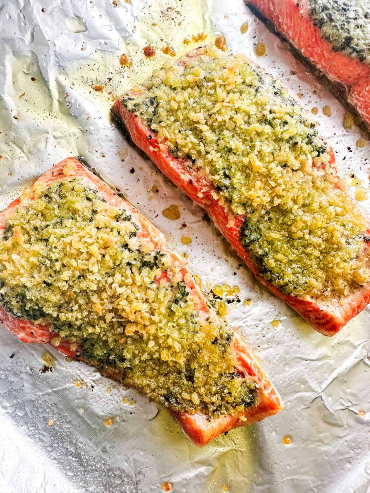 Baked pesto-crusted salmon filets on a baking sheet with aluminum foil.