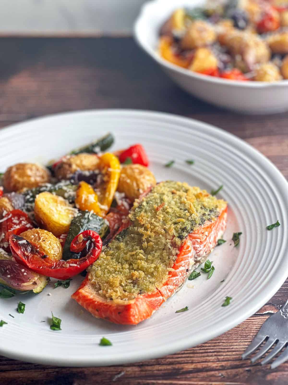 Pesto crusted salmon on a white plate with Italian roasted vegetables.