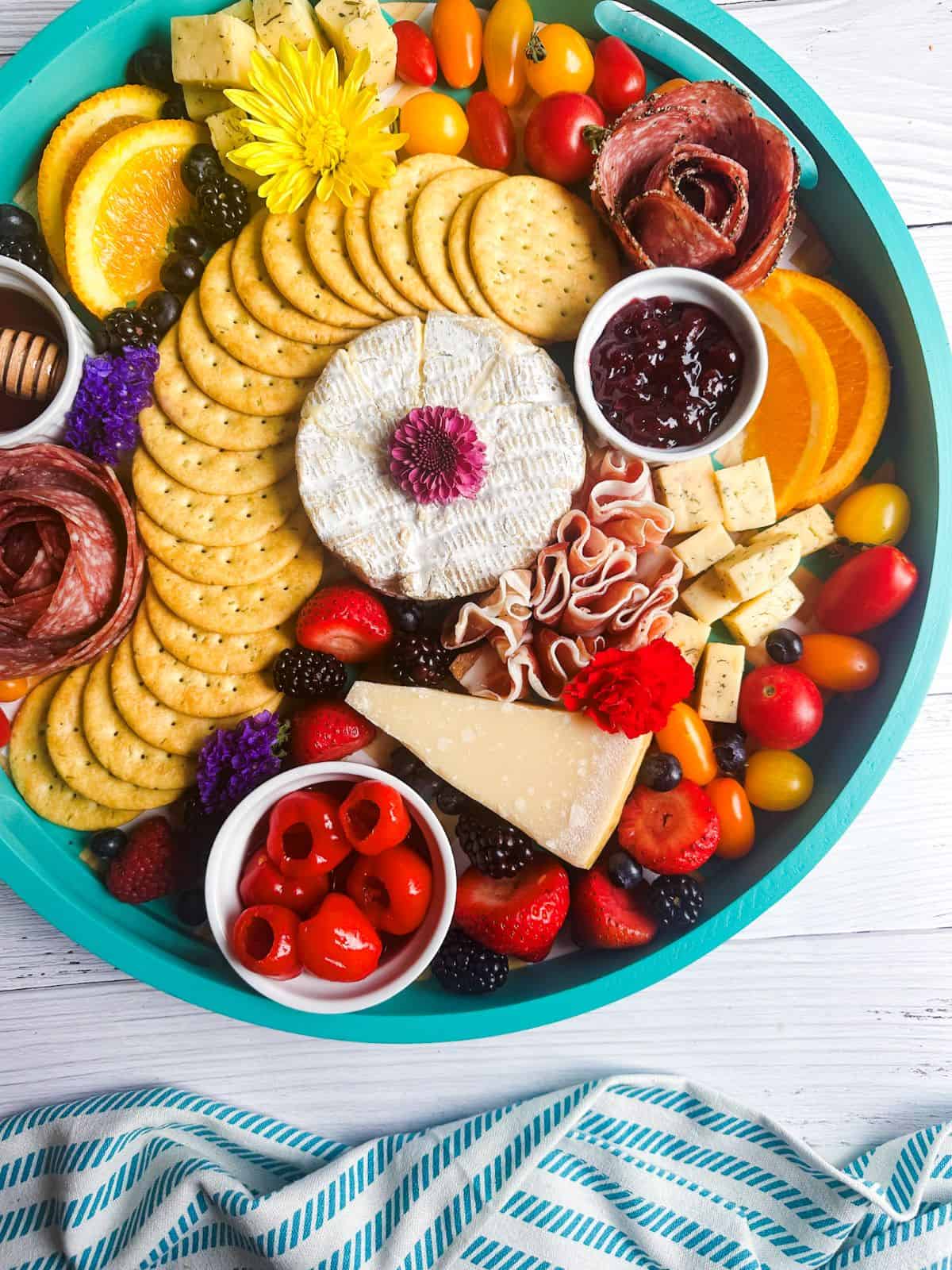 Blue charcuterie board with cheese, crackers, fruits, and veggies.