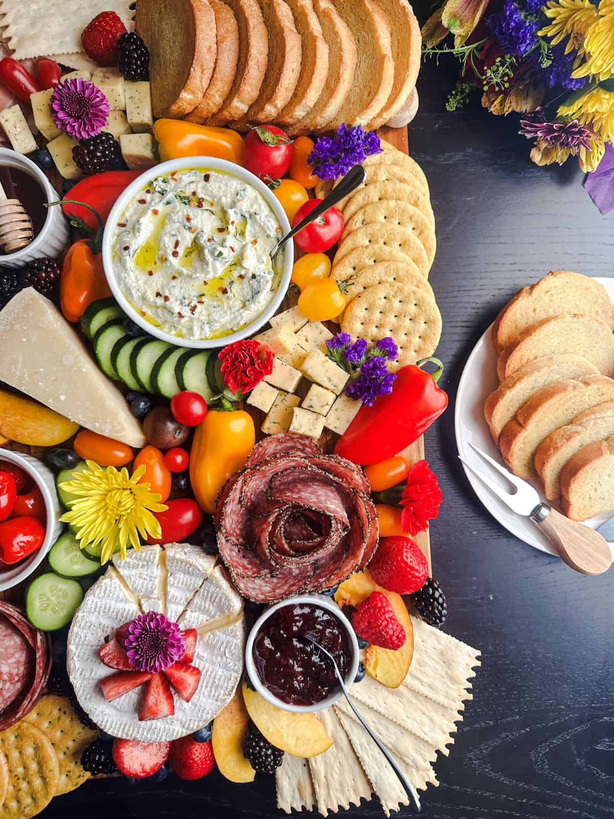 Summer charcuterie board with ricotta dip and flowers on the side.