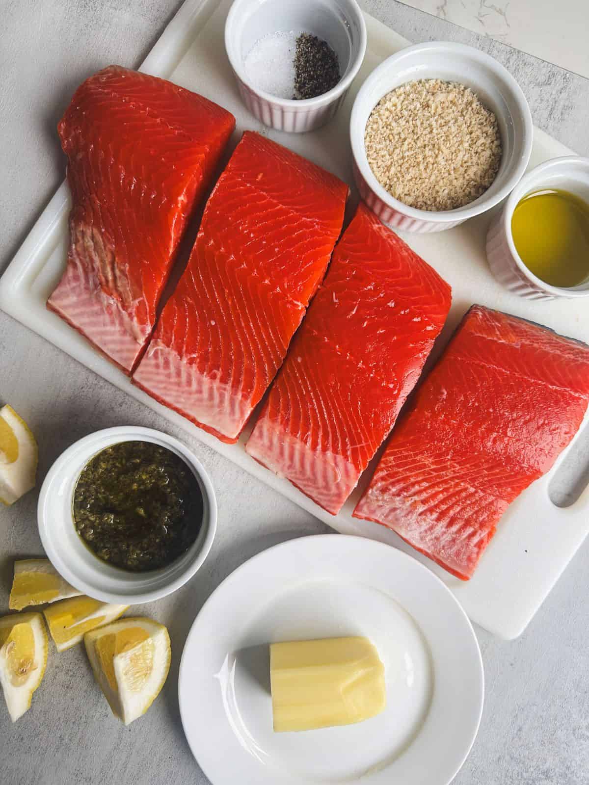 Salmon, pesto, panko, butter, lemon, olive oil, salt and pepper laid out to prepare for making pesto crusted salmon.