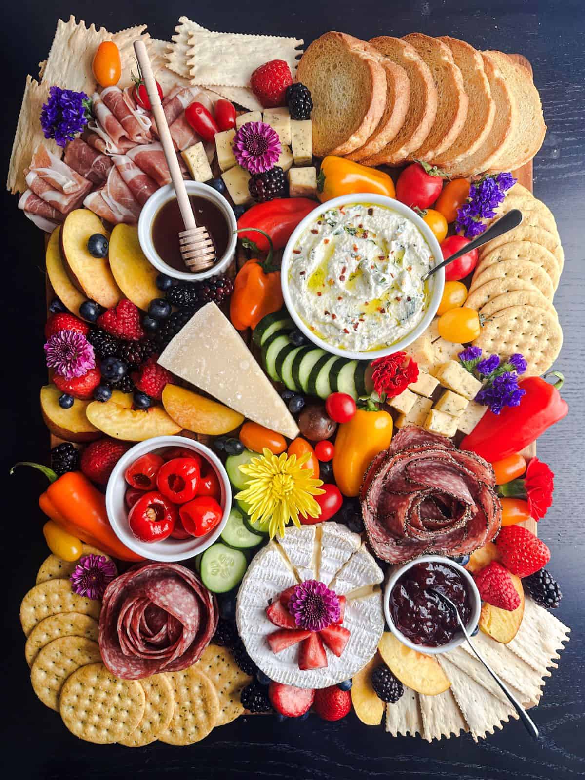 Summer-themed charcuterie board with berries, nectarines, mini peppers, cucumbers, cherry tomatoes and flowers.
