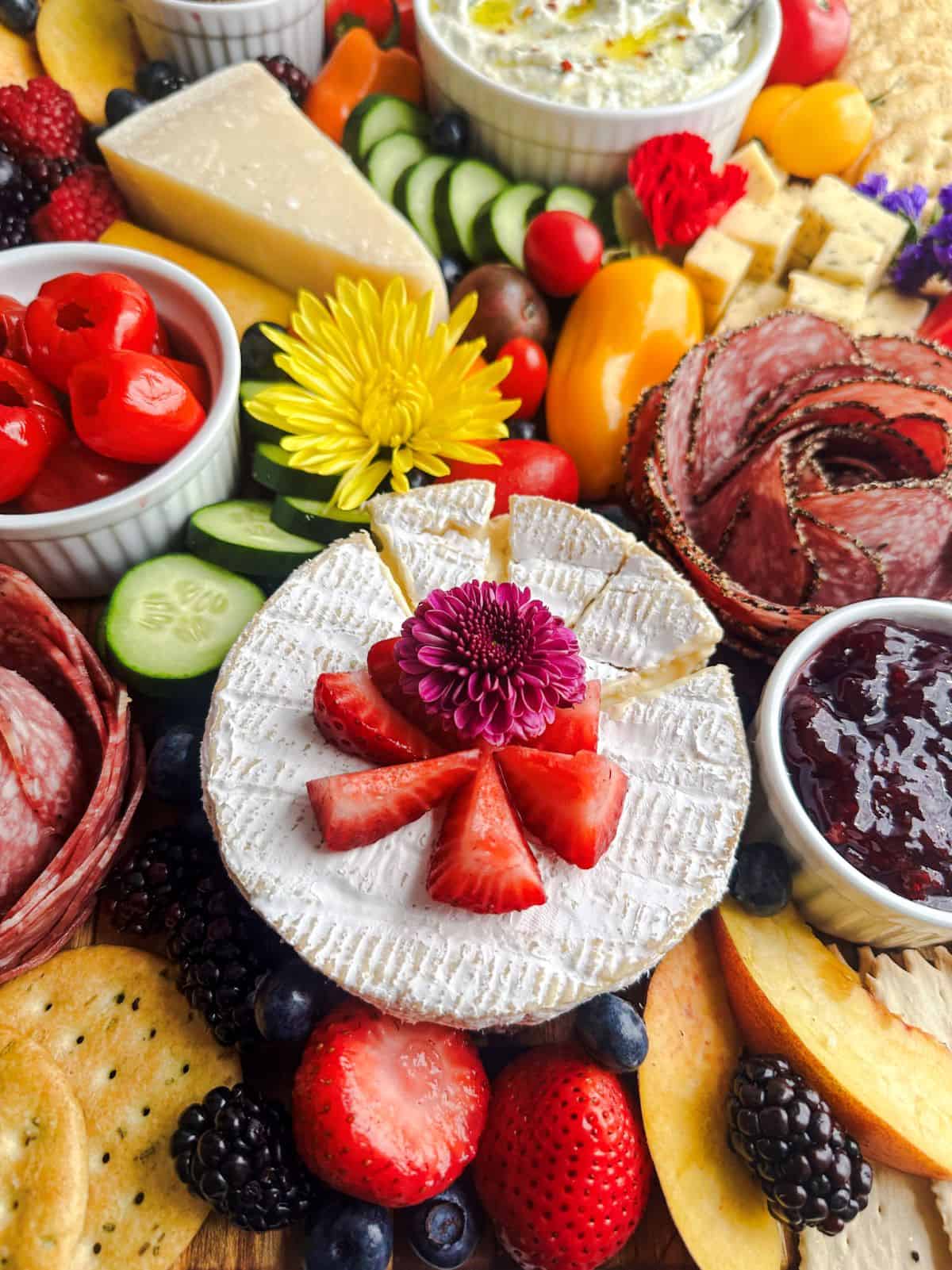 Wheel of brie on a summer charcuterie board with flowers and fruit.