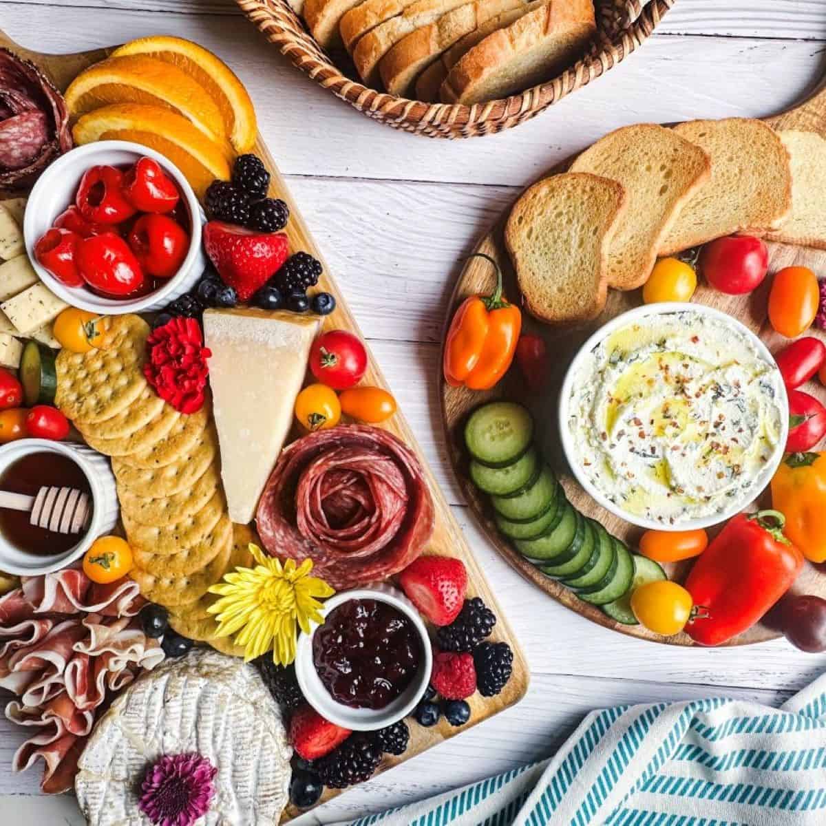 A rectangular charcuterie board and a round board with dip, veggies, and crostini.