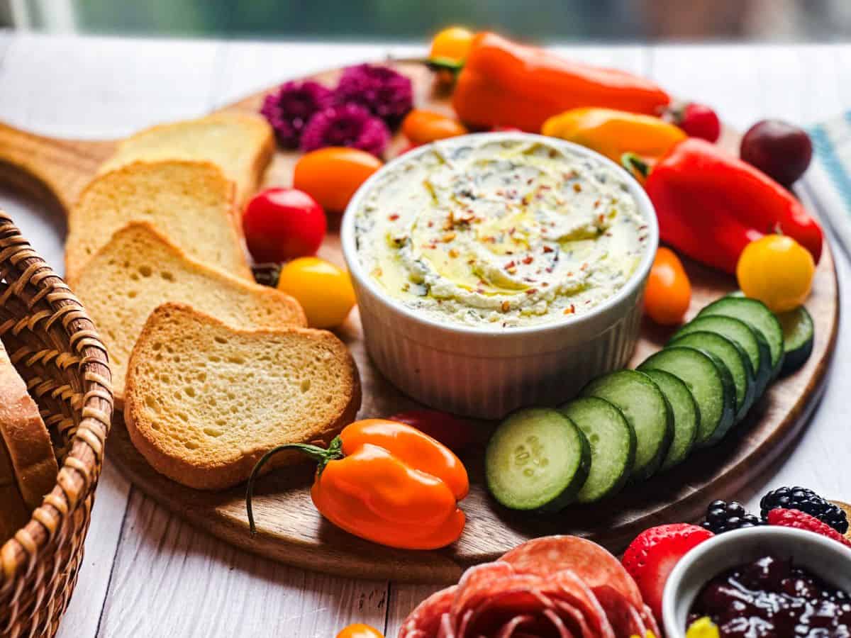 Whipped ricotta dip in a ramekin on a wooden charcuterie board with veggies.