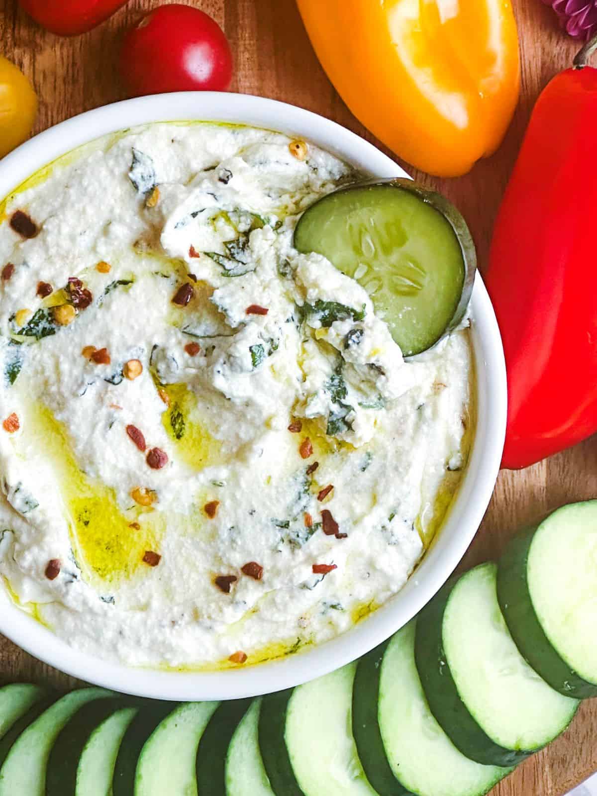 Whipped ricotta dip on a board with cucumber slices, tomatoes, and mini peppers.