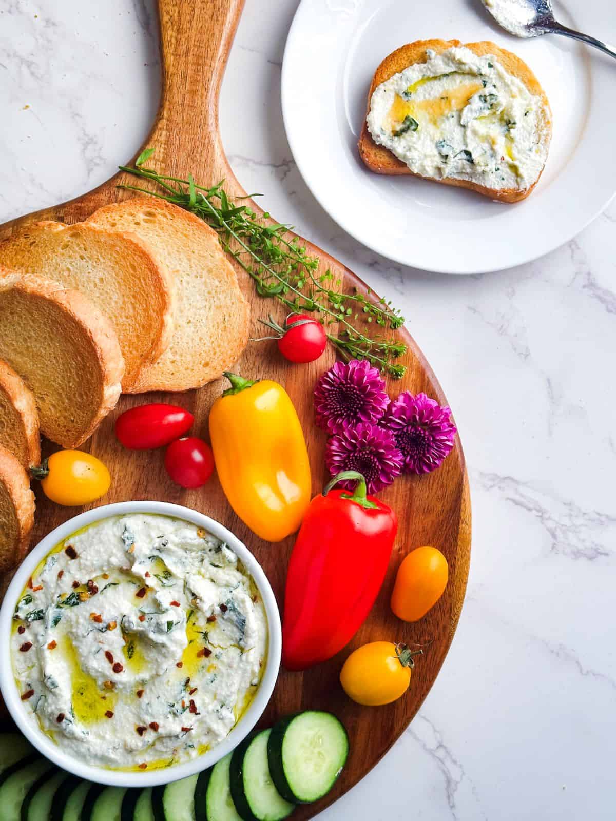 Whipped ricotta dip in a ramekin on a wooden charcuterie board with crostini.