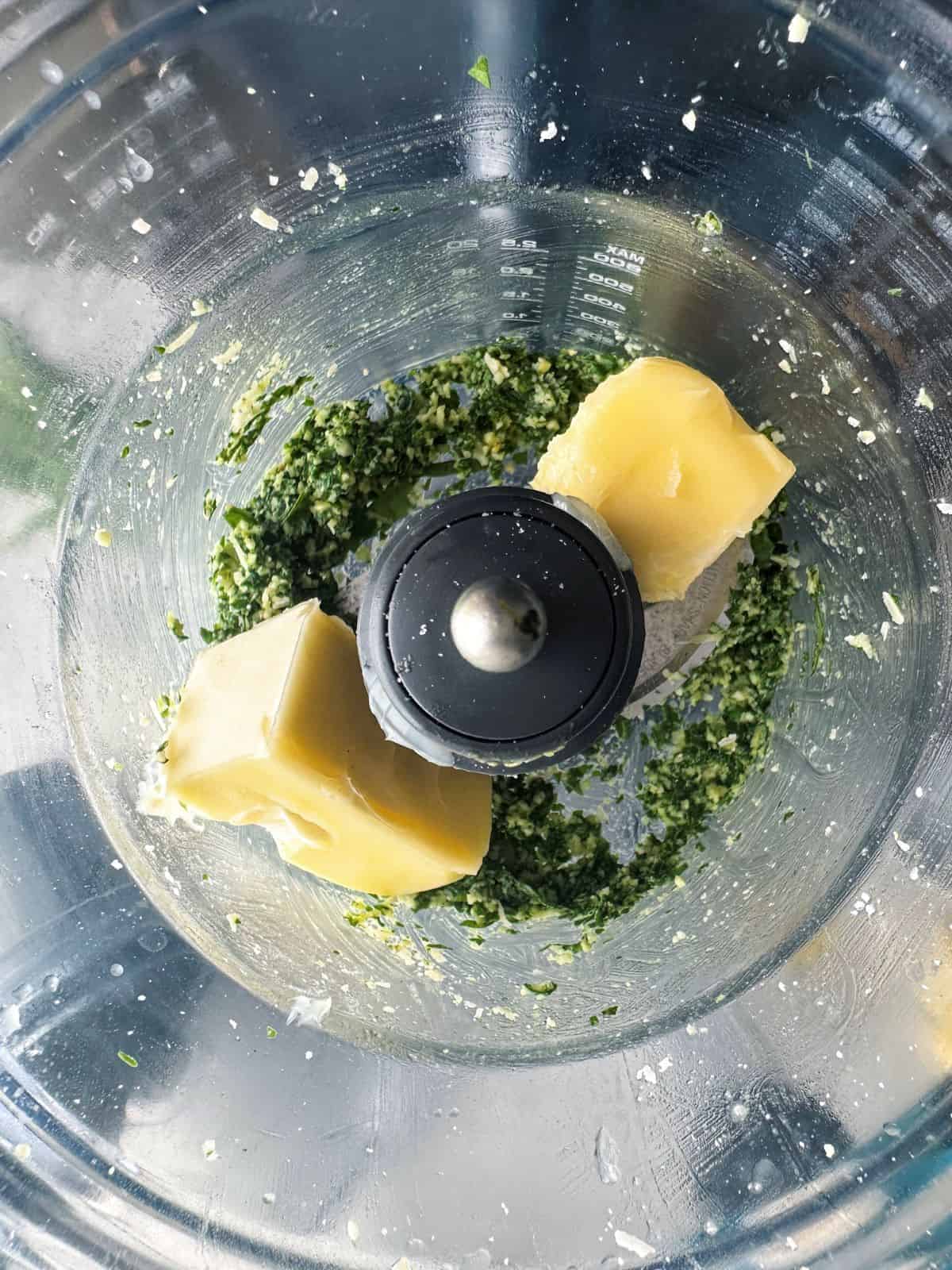Pesto and sticks of butter in a food processor bowl.