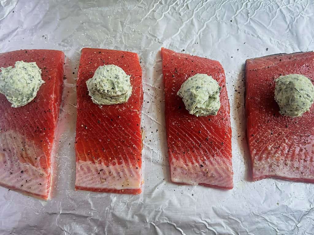 Salmon fillets topped with small scoops of pesto butter on a baking sheet.