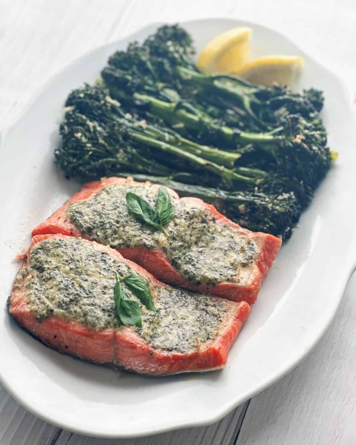 Pesto butter salmon and broccolini on a white serving plate.