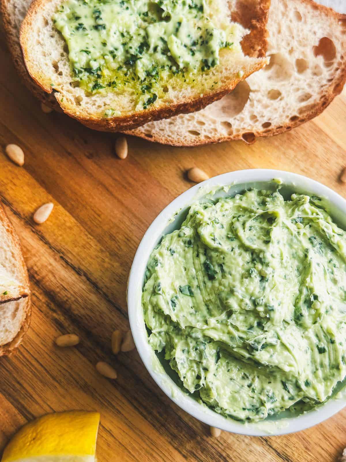 Pesto butter on a serving board with slices of bread.