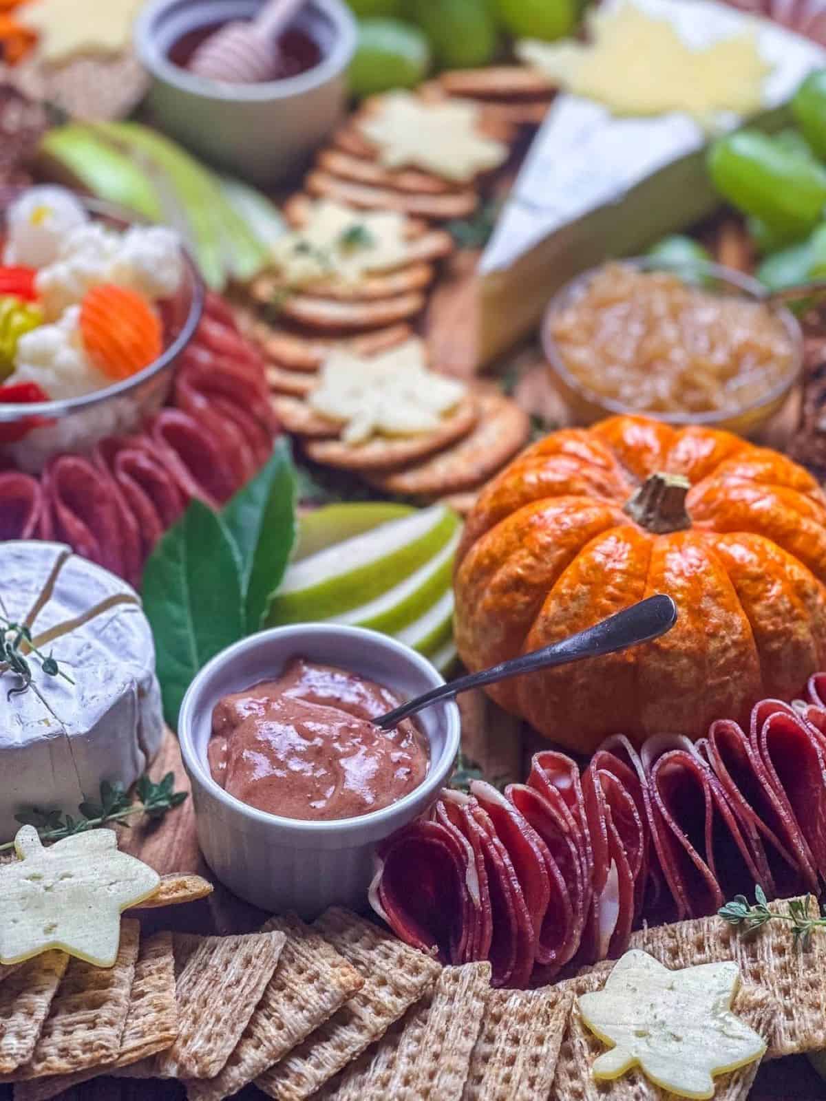 Cranberry honey mustard in a ramekin on a fall charcuterie board with a mini pumpkin, whole wheat crackers, pears, and maple leaf shaped cheese slices.
