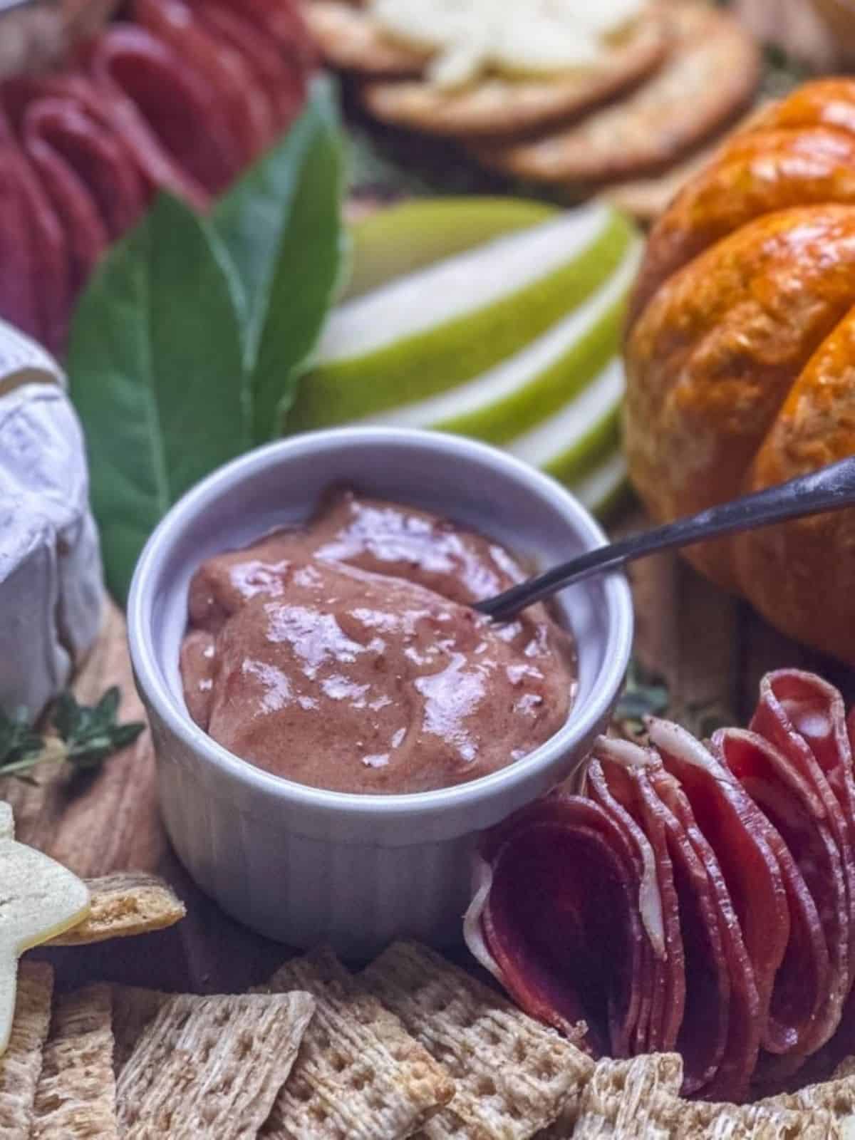 Cranberry honey mustard in a ramekin on a fall charcuterie board with crackers, meats, pear, and cheeses.