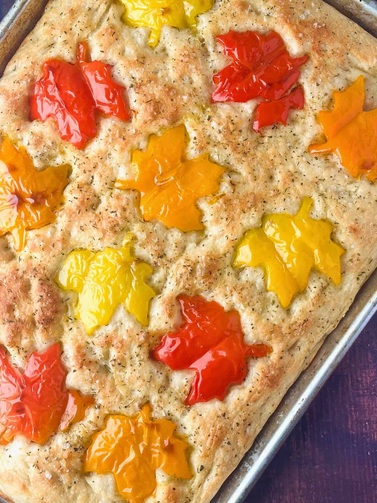 Fall focaccia art style bread topped with maple leaf shaped red, orange, and yellow bell peppers.