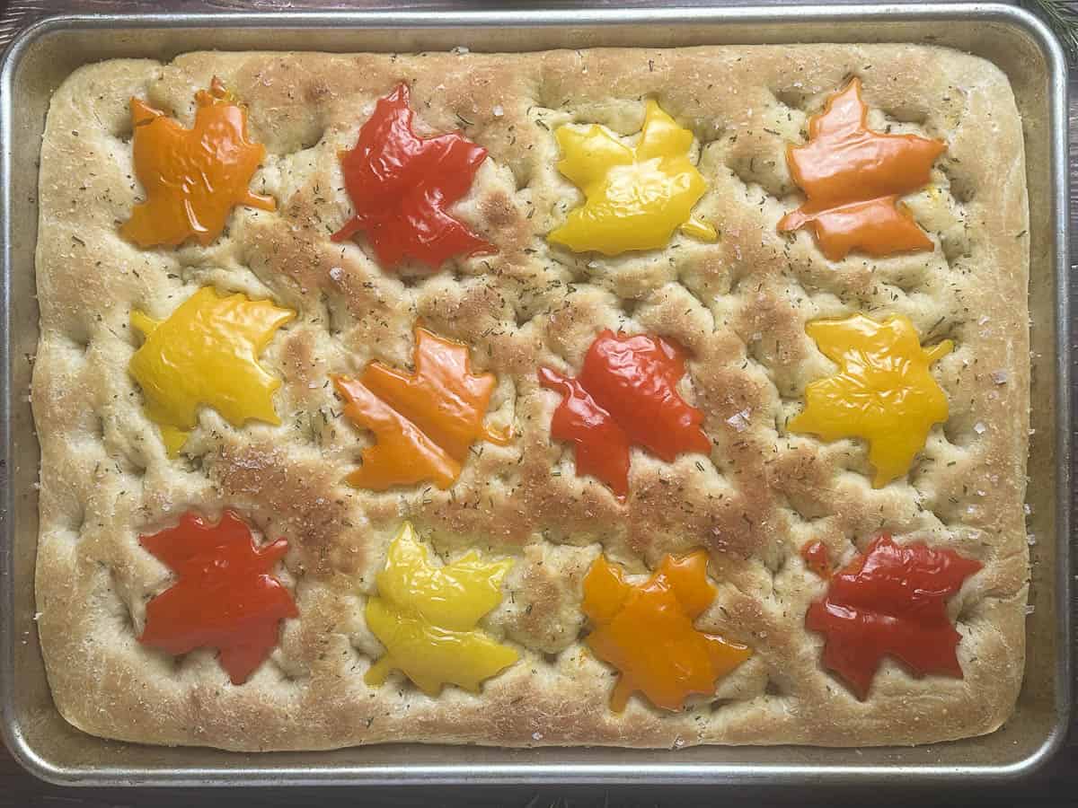Fall focaccia bread topped with maple leaf shaped bell peppers on a baking sheet.