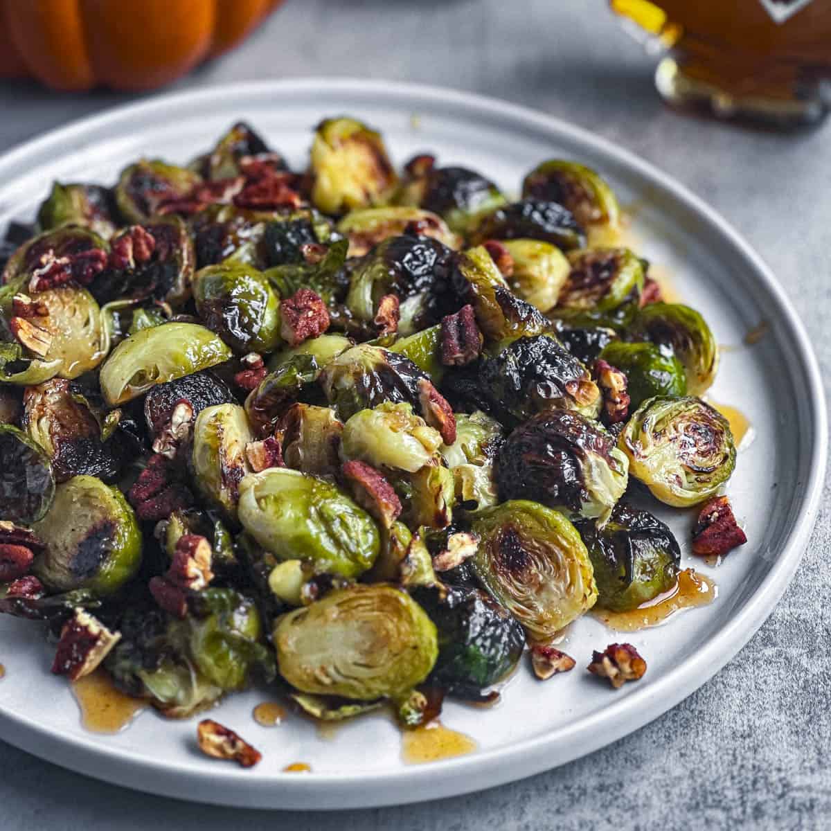 Roasted brussels sprouts on a round white plate with pecans.