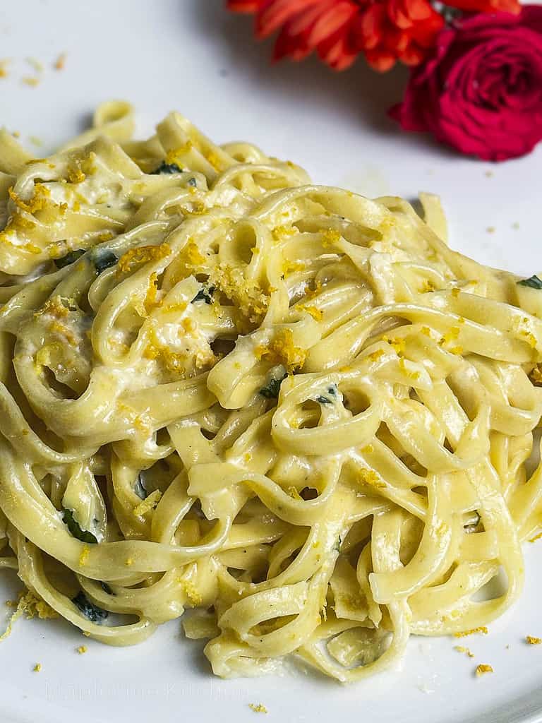 Pasta magnifico - linguine tossed in a citrus cream sauce - on a white plate with fresh flowers for garnish.