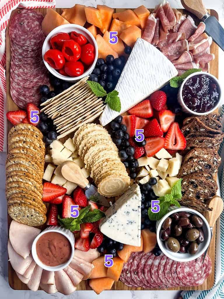 Charcuterie board with step number 5 labels for filling the gaps with fruits.