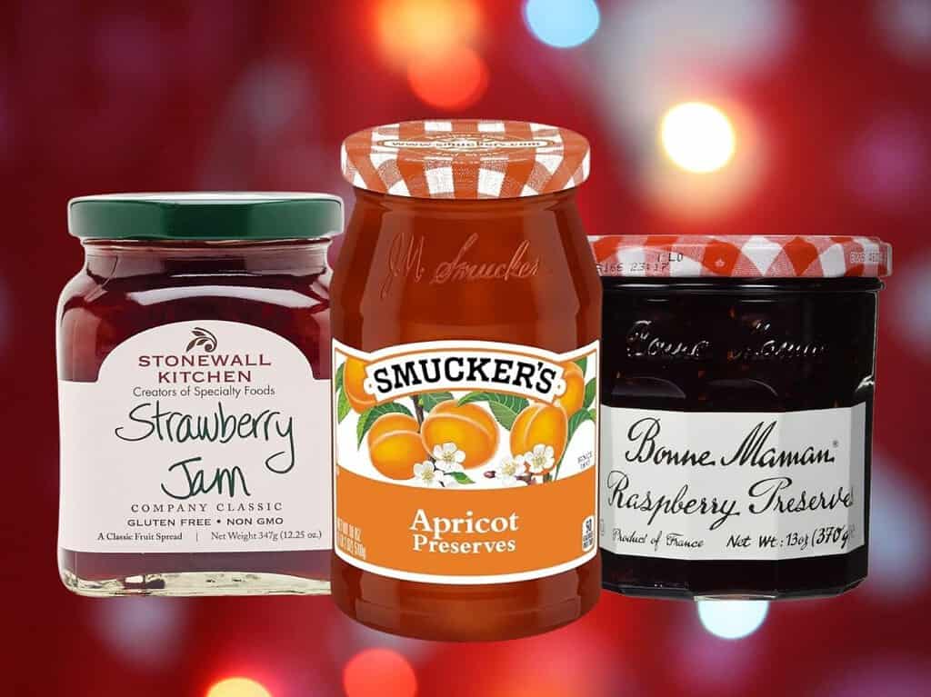 Jars of strawberry jam and apricot and raspberry preserves on a red background.
