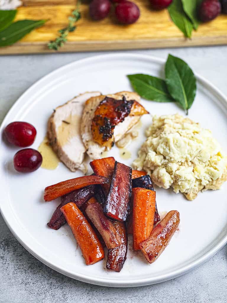 Hot honey carrots on a white dinner plate with turkey and mashed potatoes.