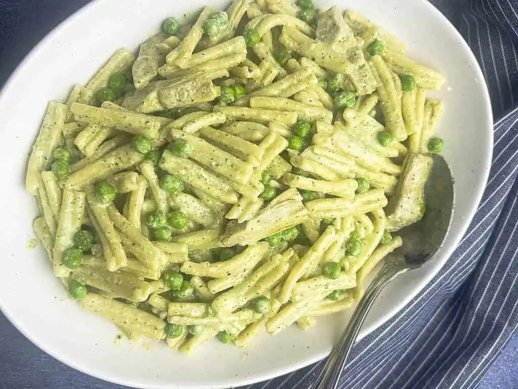 Ricotta pesto pasta with peas and artichokes on a white serving plate with a spoon.