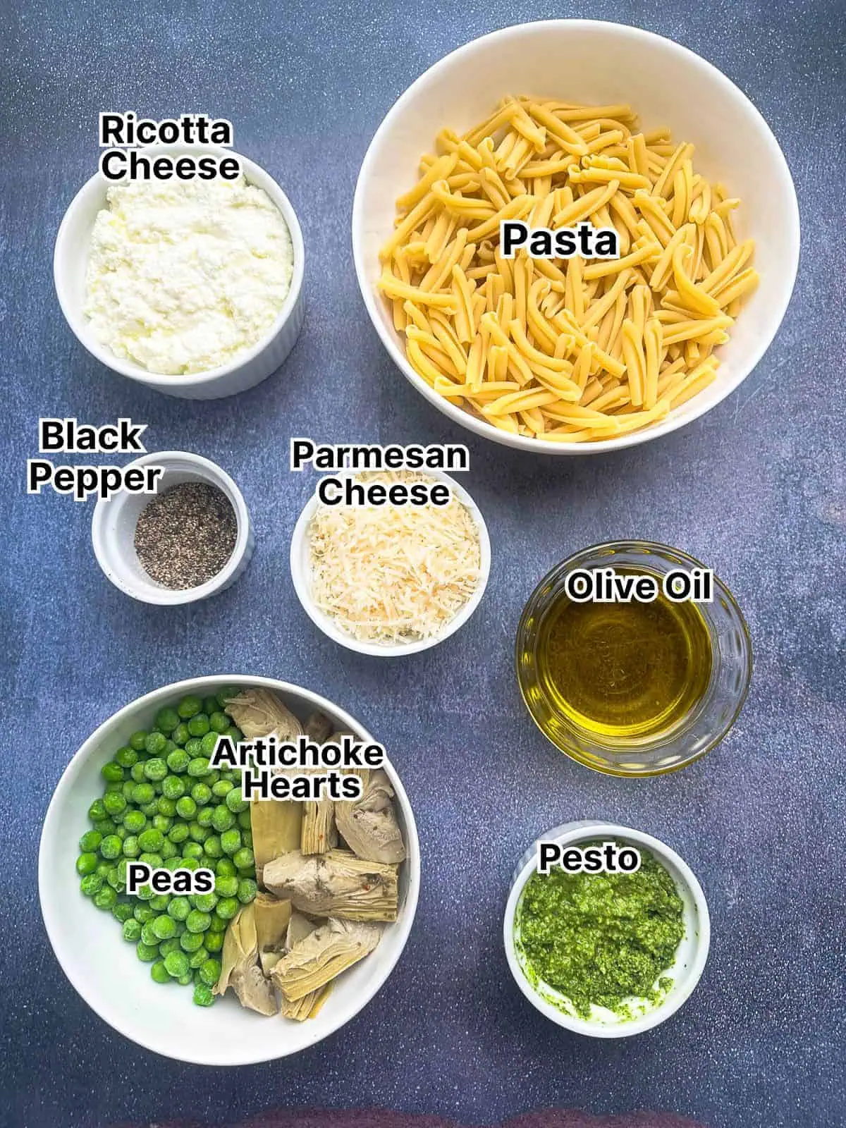 Ricotta pesto pasta ingredients laid out into small white bowls and dishes on a dark gray surface.