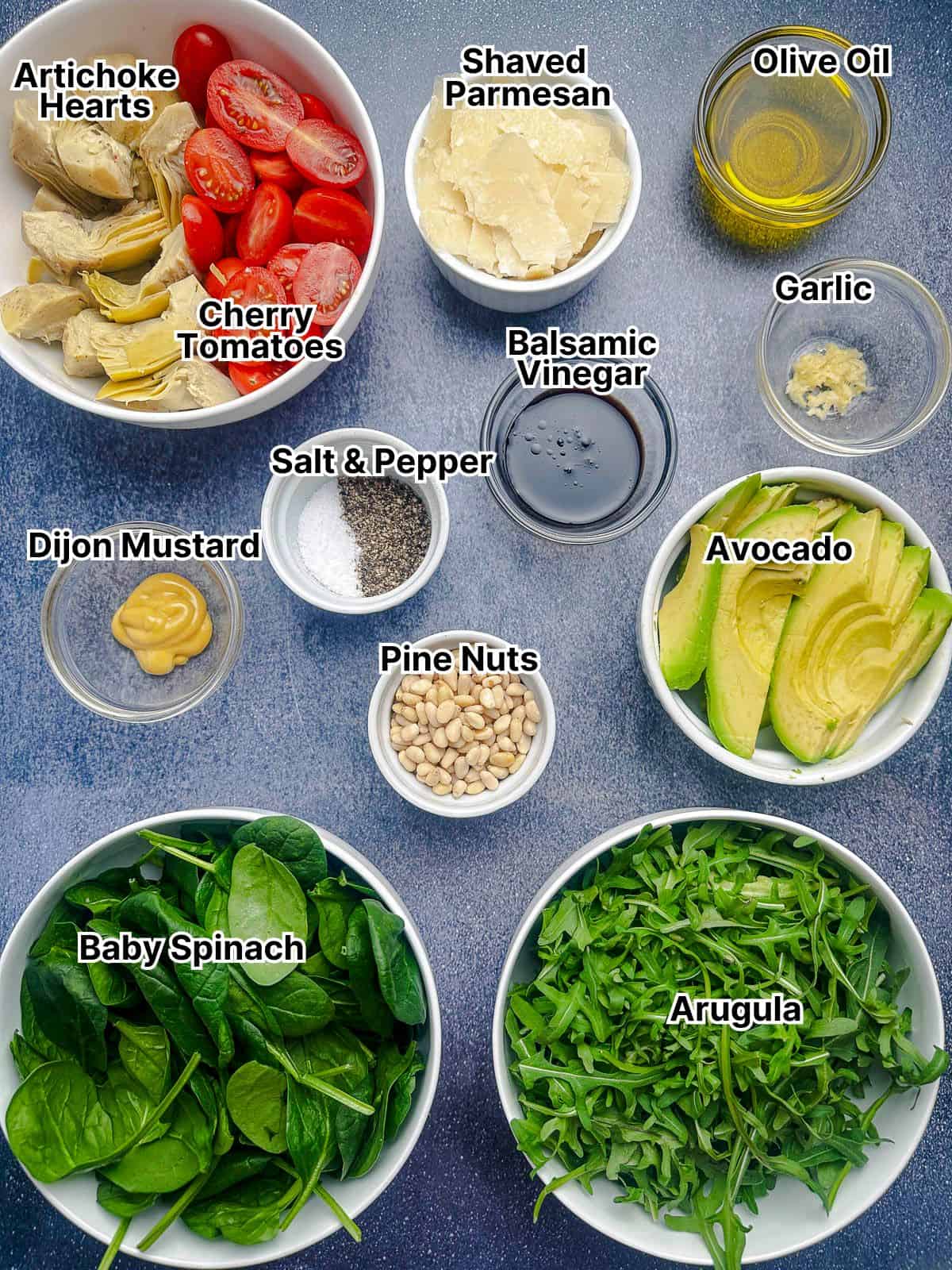 Ingredients for spinach and arugula salad displayed in small bowls with labels.