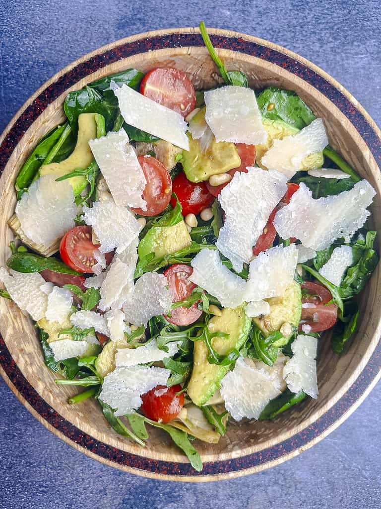 Spinach and arugula salad with shaved parmesan in a wooden salad bowl.