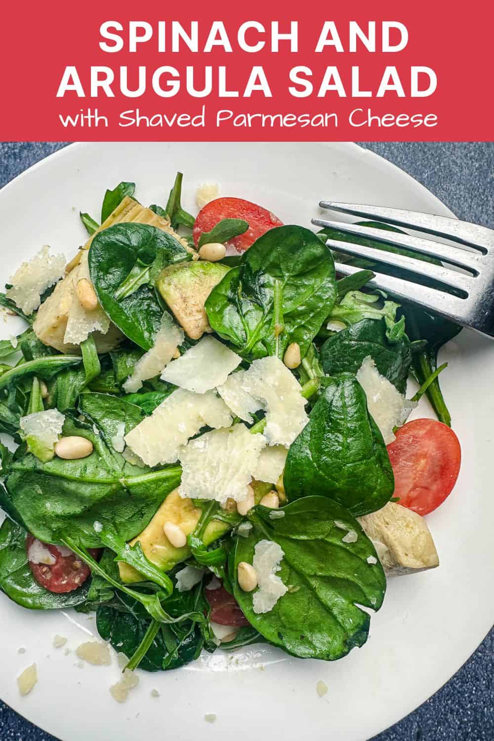 Spinach and arugula salad with shaved parmesan on a white plate.