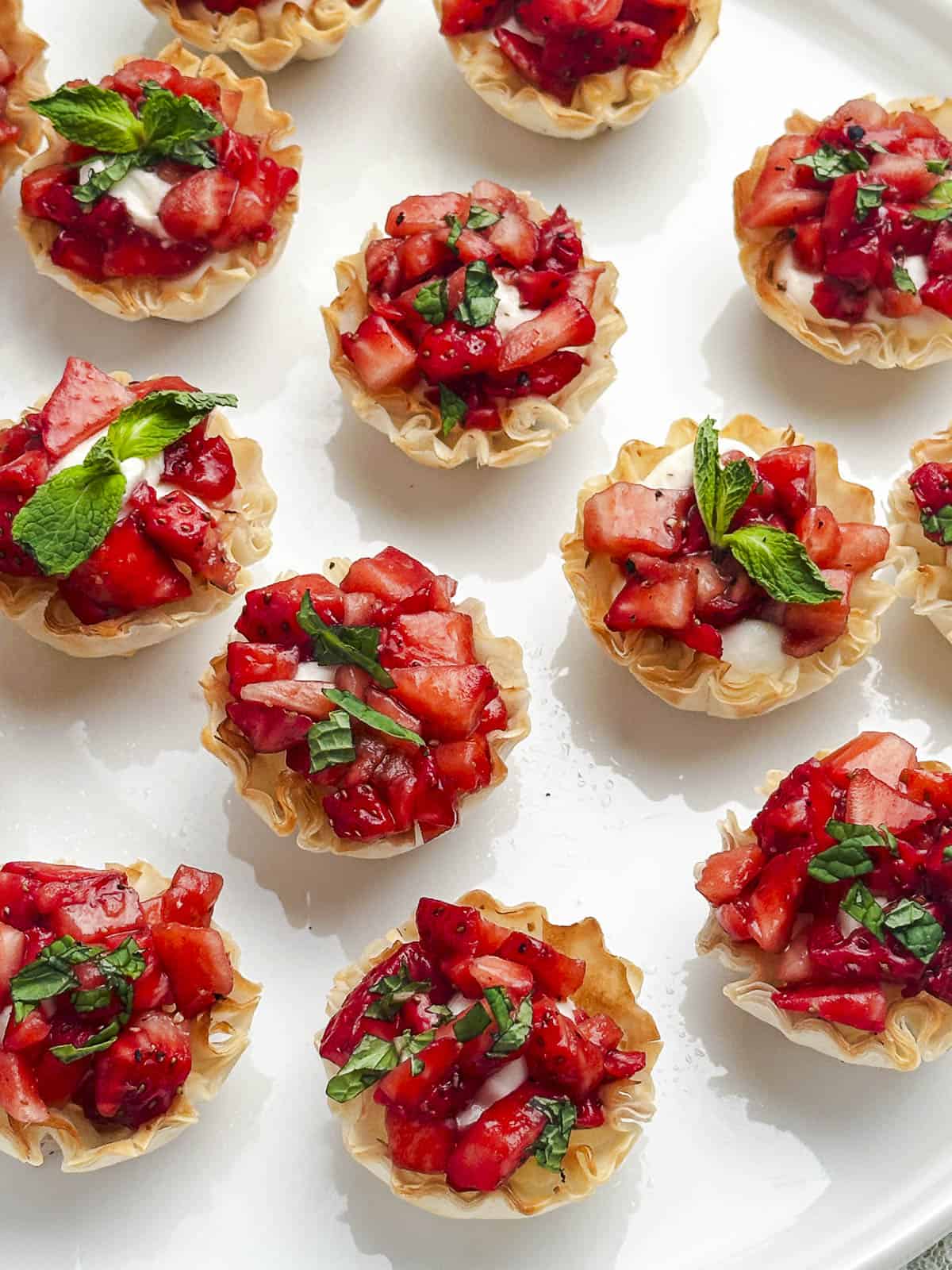 Goat cheese phyllo cups with balsamic marinated strawberries topped with fresh mint on a white plate.