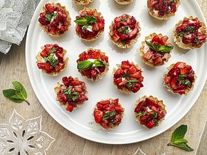 Goat cheese filo cups with balsamic honey strawberries topped with fresh mint on a white plate inside a wooden tray.