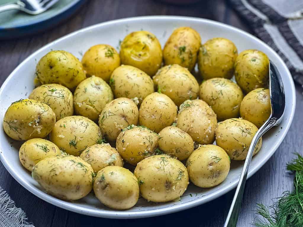 Buttered new potatoes with dill, garlic, and lemon on a white oval plate.