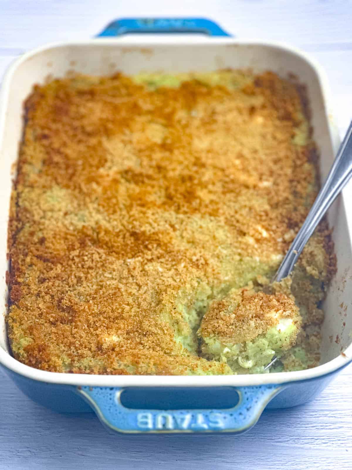 Pesto mashed potatoes au gratin in a casserole dish with a scoop of the gratin on a serving spoon.