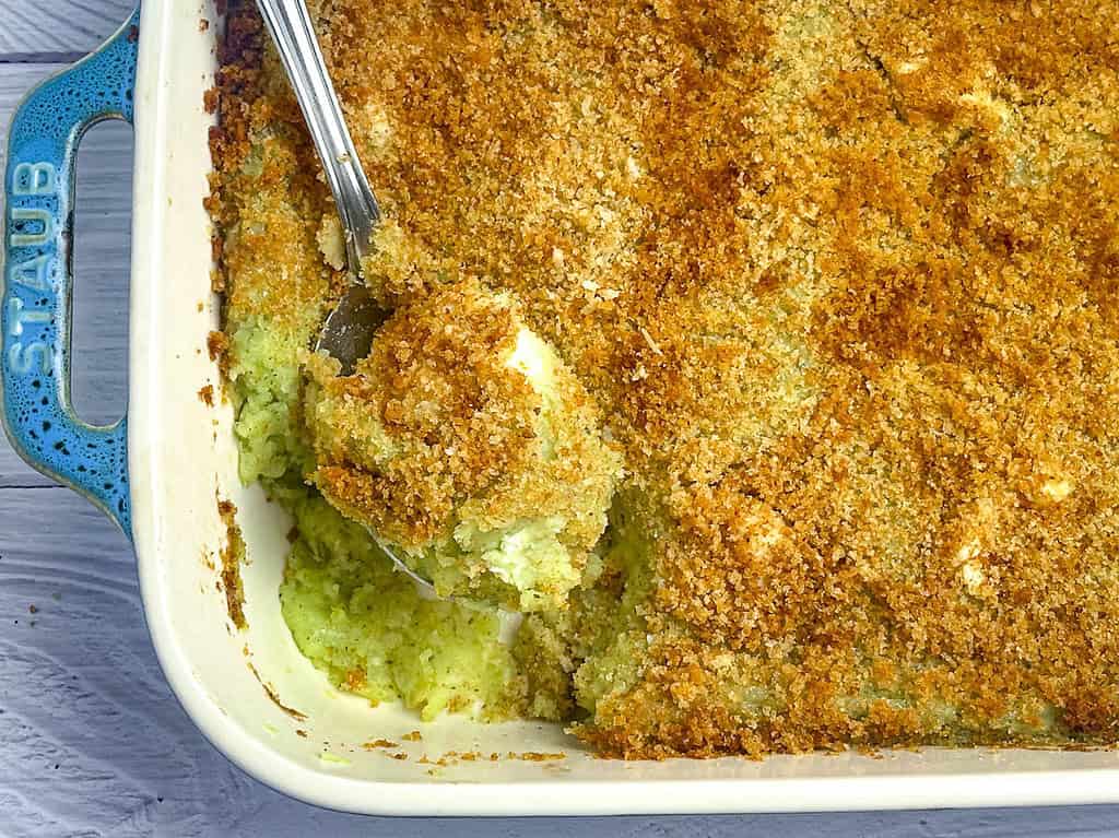 Pesto mashed potatoes au gratin in a Staub baking dish with a serving spoon.