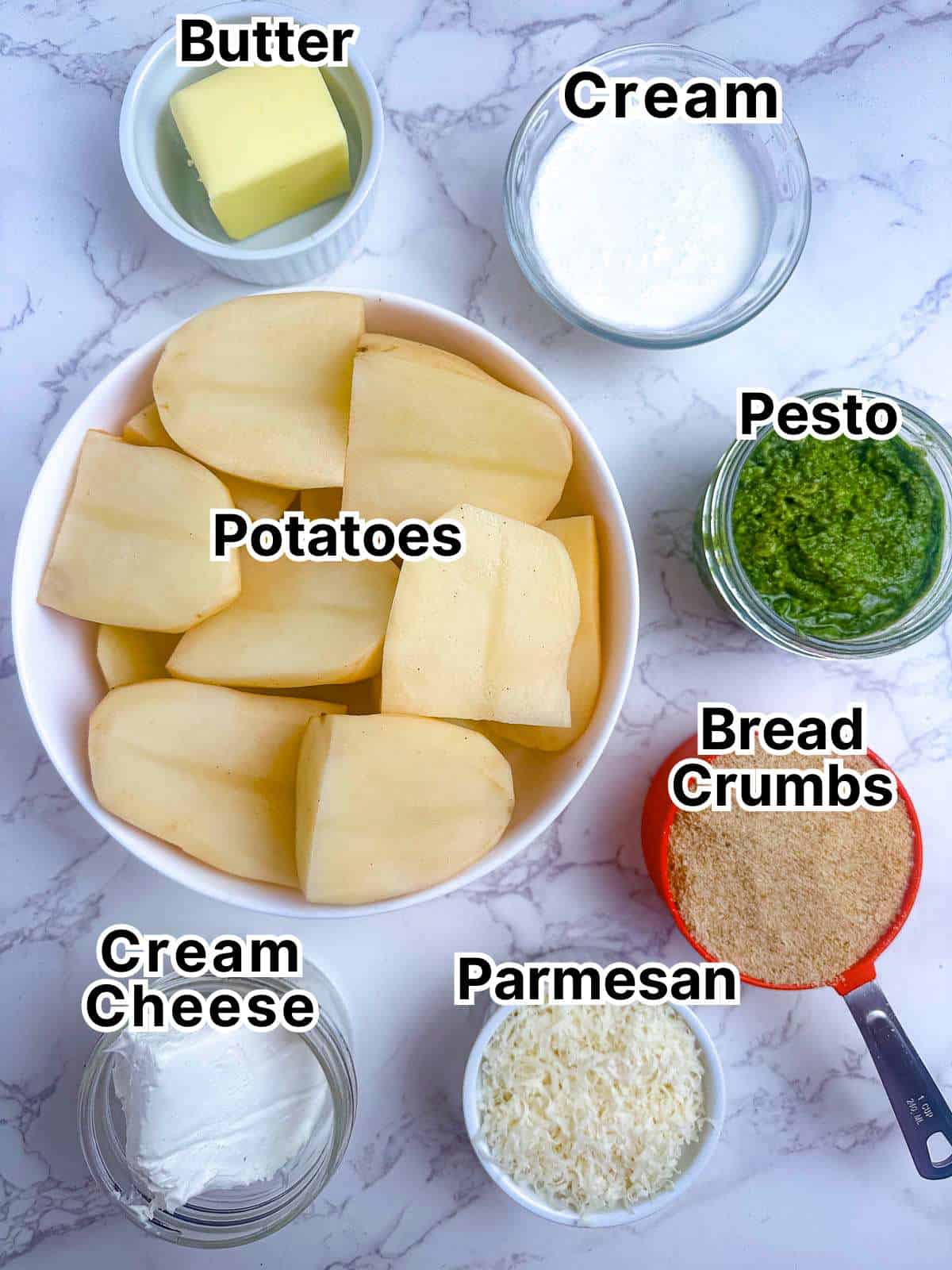 Ingredients for pesto mashed potatoes au gratin laid out on a marble counter in small bowls and ramekins.