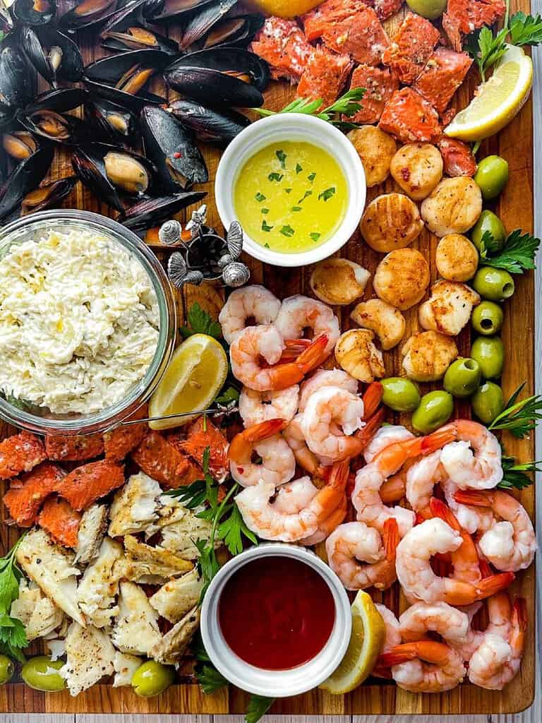 Prawns, salmon, scallops and mussels on a wooden cutting board with dipping sauces.