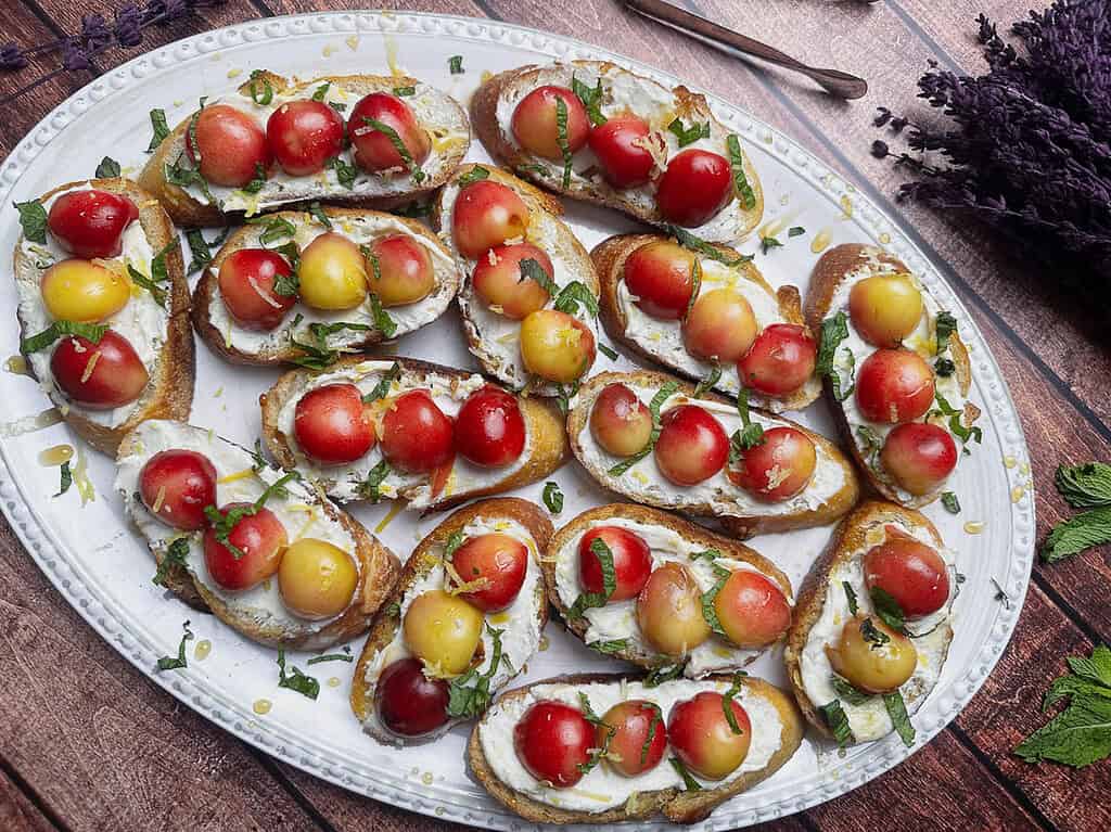 Goat cheese crostini with Rainier cherry halves on a white oval platter.