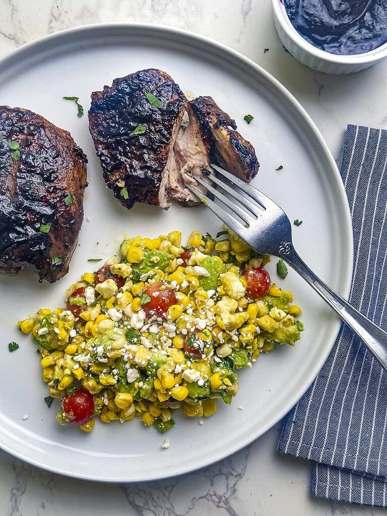 Blueberry barbecue chicken with charred corn salad on a white plate.