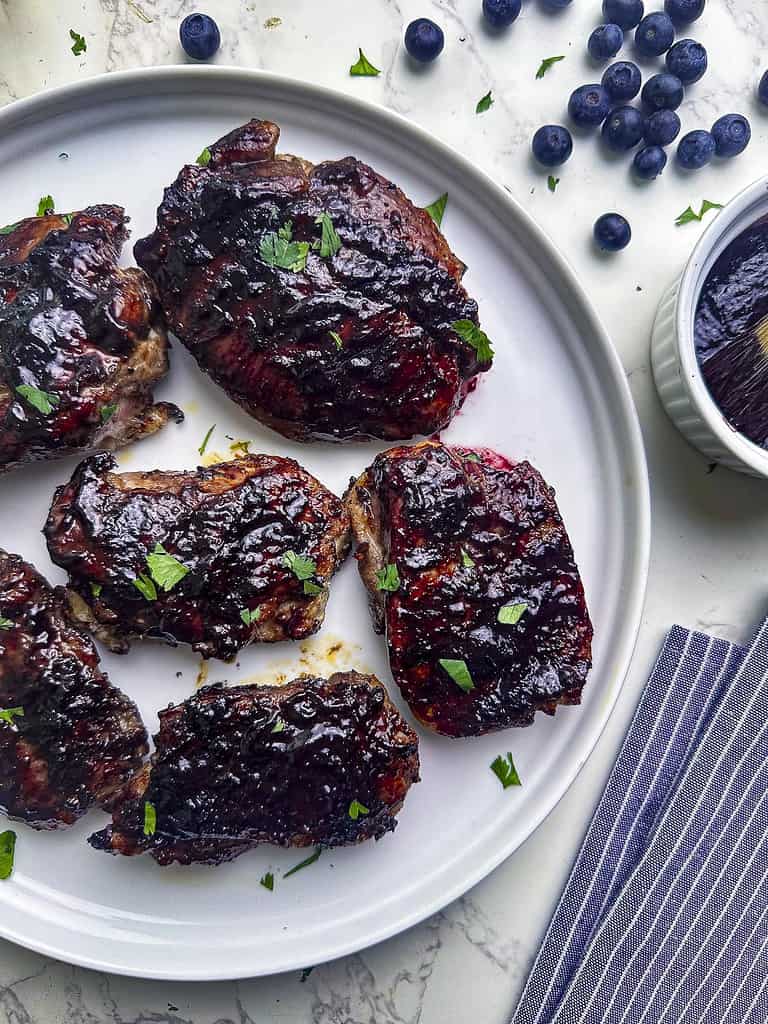 Grilled chicken thighs with blueberry barbecue sauce on a plate.