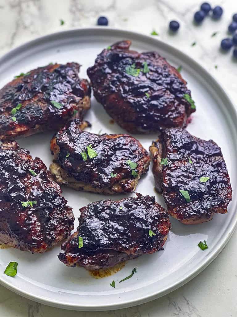 Blueberry barbecued chicken thighs on a white round plate.