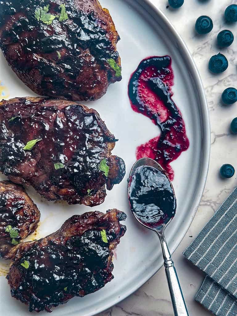 Grilled chicken on plate with a spoon of blueberry BBQ sauce.