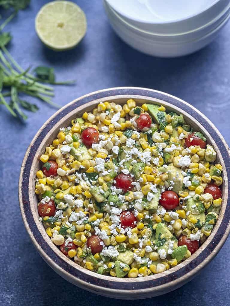 Charred corn salad in a wood bowl with tomatoes, avocado, and feta.