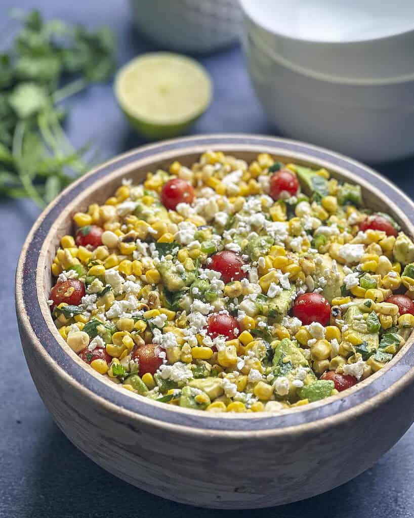 Charred corn salad in a bowl with lime and cilantro on the side.