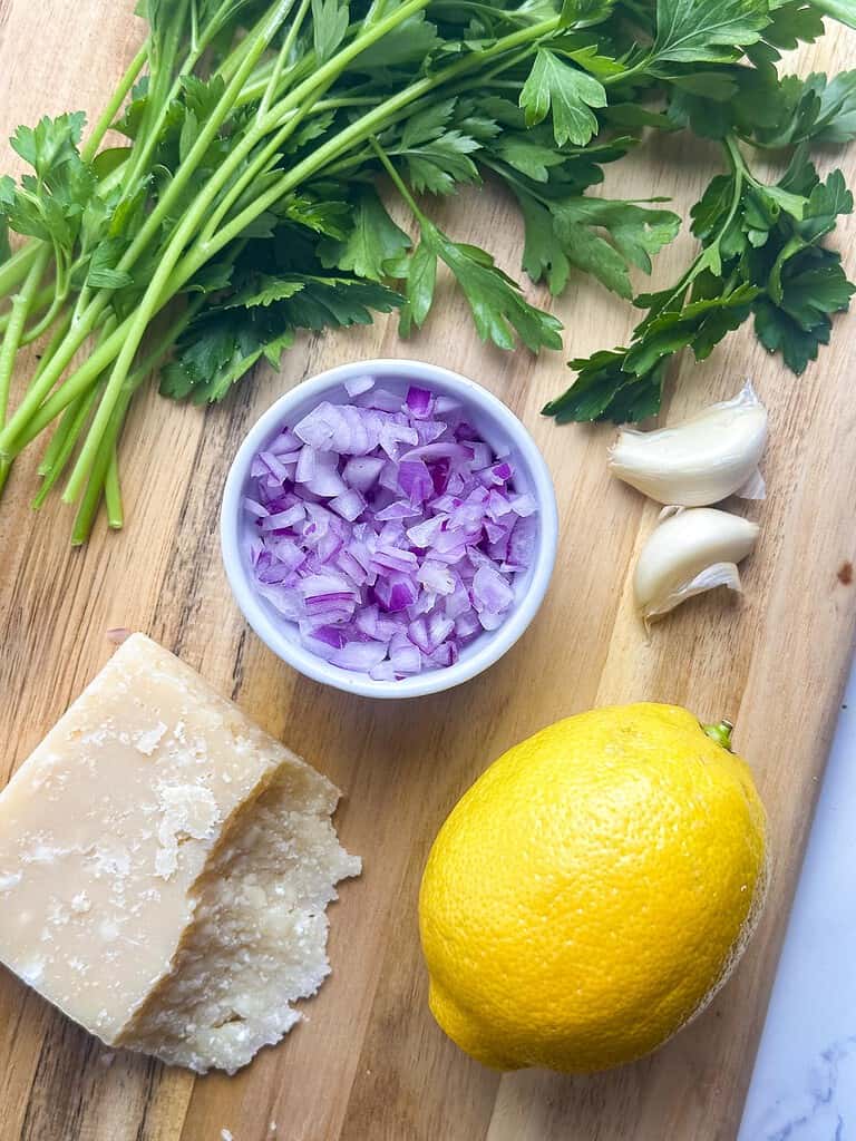 Lemon, parmesan cheese, onion, parsley, and garlic on a wood cutting board.