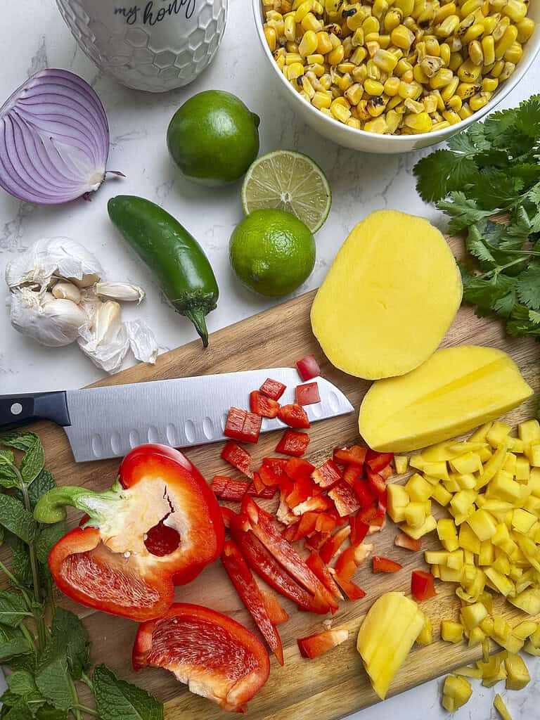 Mango, bell pepper, corn and the other ingredients laid out on a cutting board.