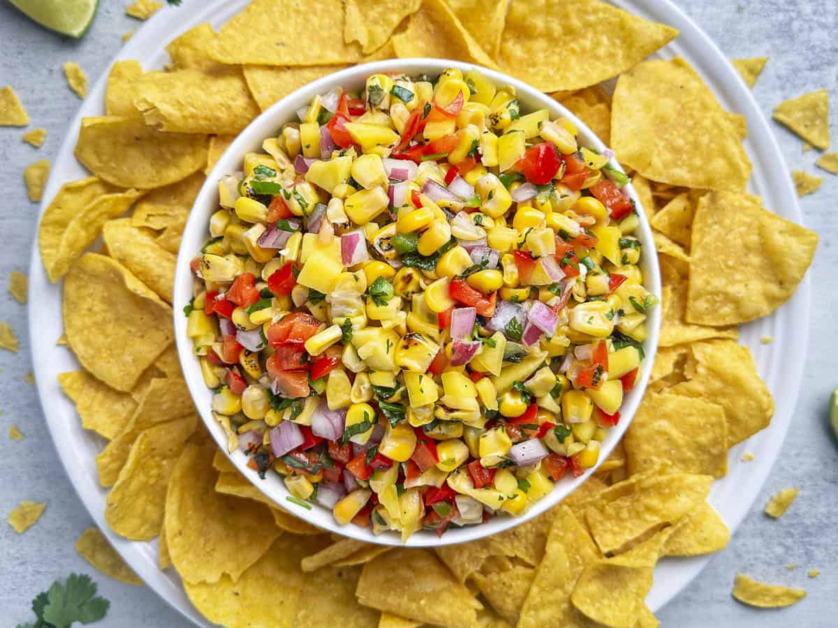 Mango corn salsa in a bowl with tortilla chips on a white plate.