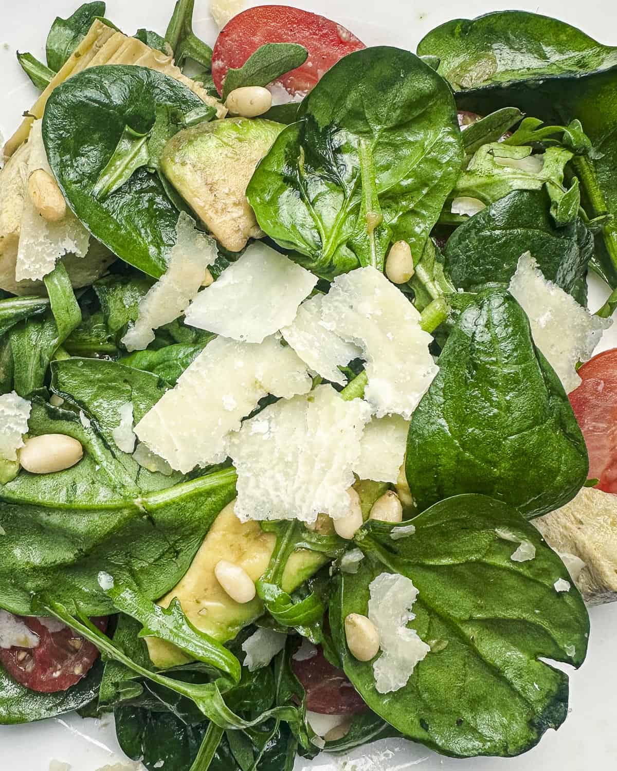 Close up shot of spinach arugula salad with avocado, tomato, artichoke, pine nuts, and shaved Parmesan.