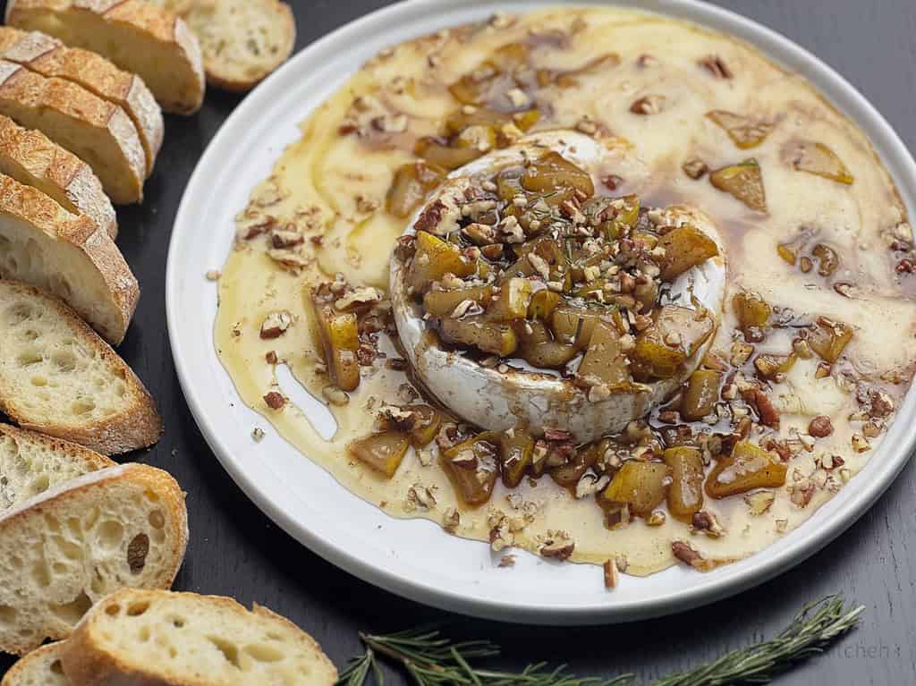 Baked brie with spiced pears and rosemary honey on a white plate.