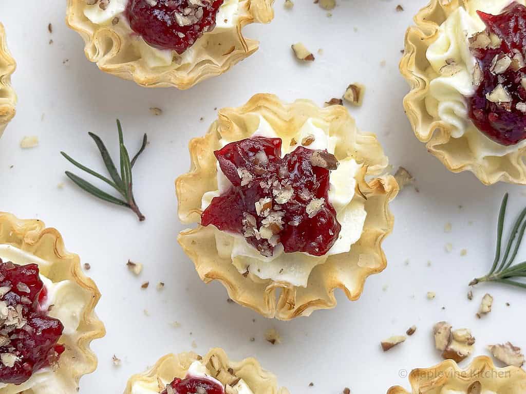 Cranberry tartlets topped with chopped pecans on a round white plate.